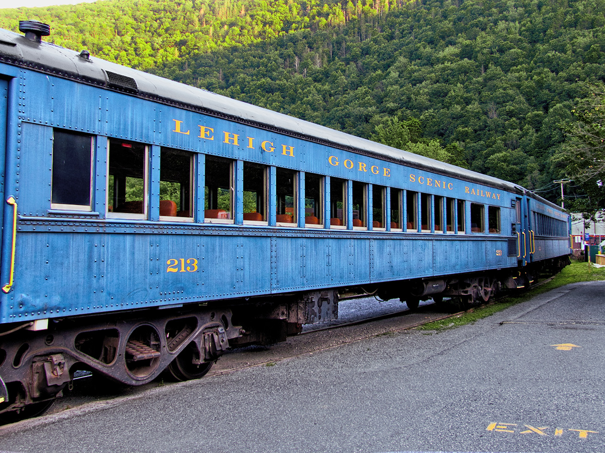 Blue Vintage Passenger Rail Car with a a tree Covered mountain in the background.