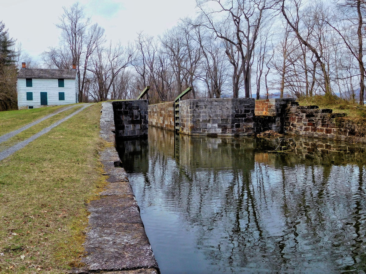 low to the ground view of a watered lock with stone block walls. White Lock house in rear left with tow path along right hand side.
